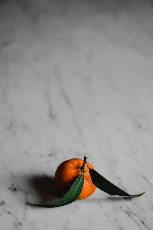 Free A single tangerine with leaves on a marble surface, showcasing minimalist still life. Stock Photo
