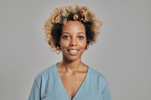Close-up portrait of a happy woman with curly hair and a nose ring against a gray background.