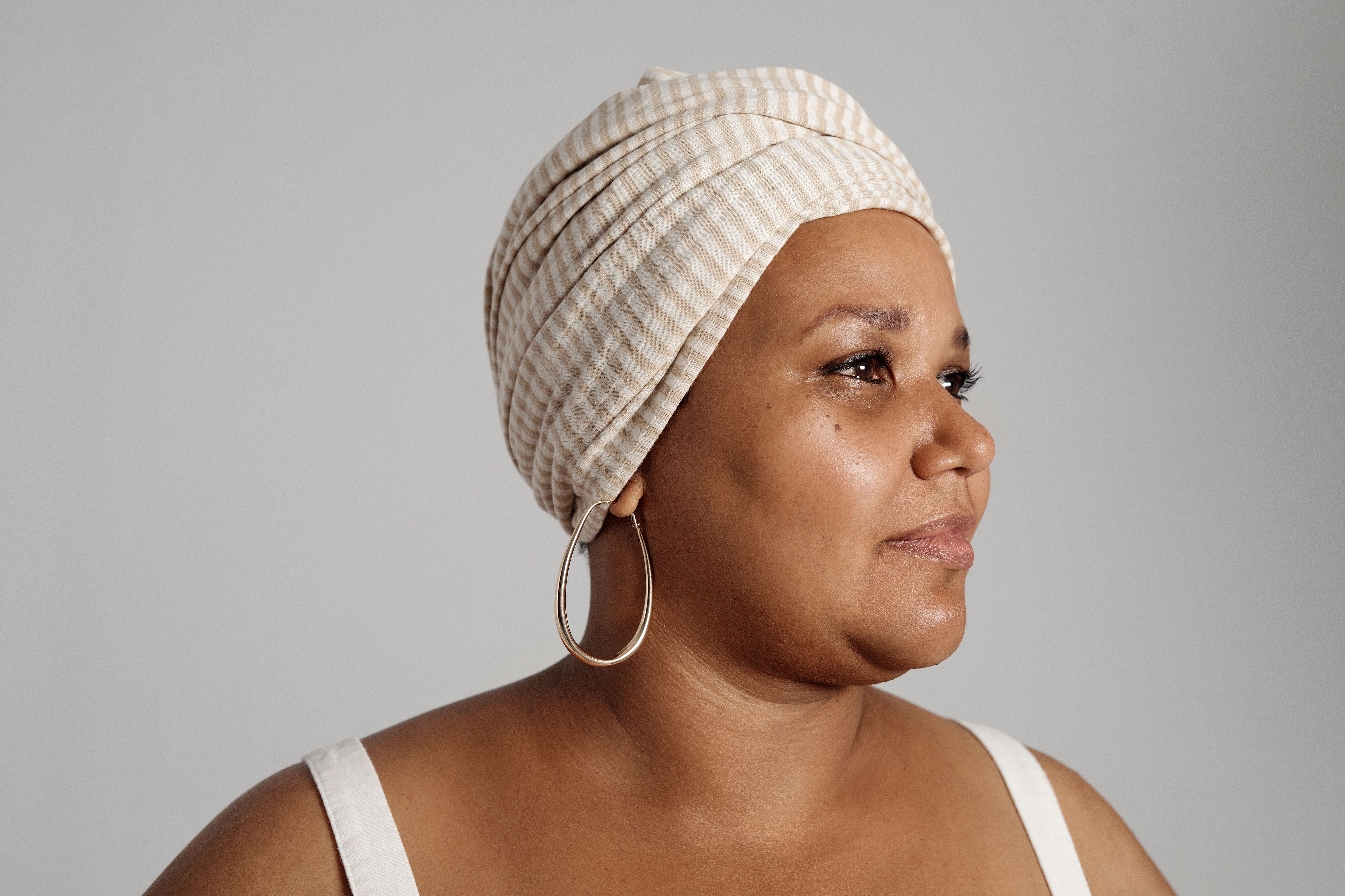 Side view portrait of a woman with a striped headwrap and hoop earrings.