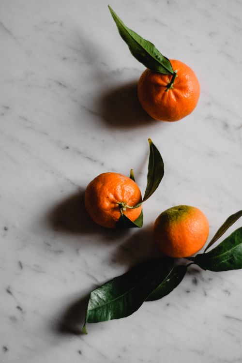 Free Three ripe oranges with leaves on a marble background in natural light. Stock Photo