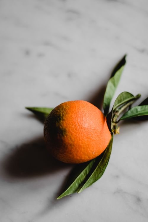 Free A close-up of a fresh orange with leaves on a marble surface, enhancing a natural look. Stock Photo