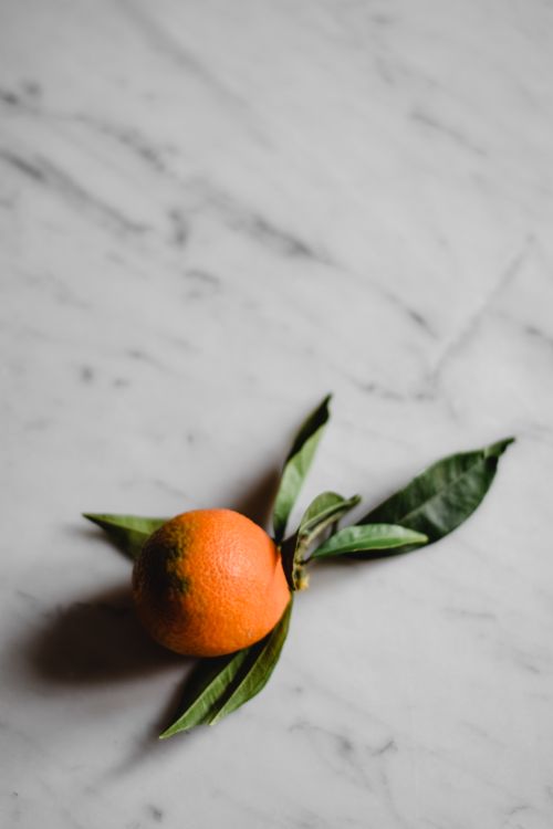 Free A fresh clementine with green leaves on a marble surface, in a minimalist setting. Stock Photo