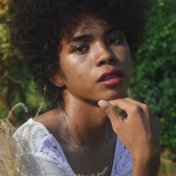 Close-up portrait of a woman with afro hair in a natural setting, contemplative mood.