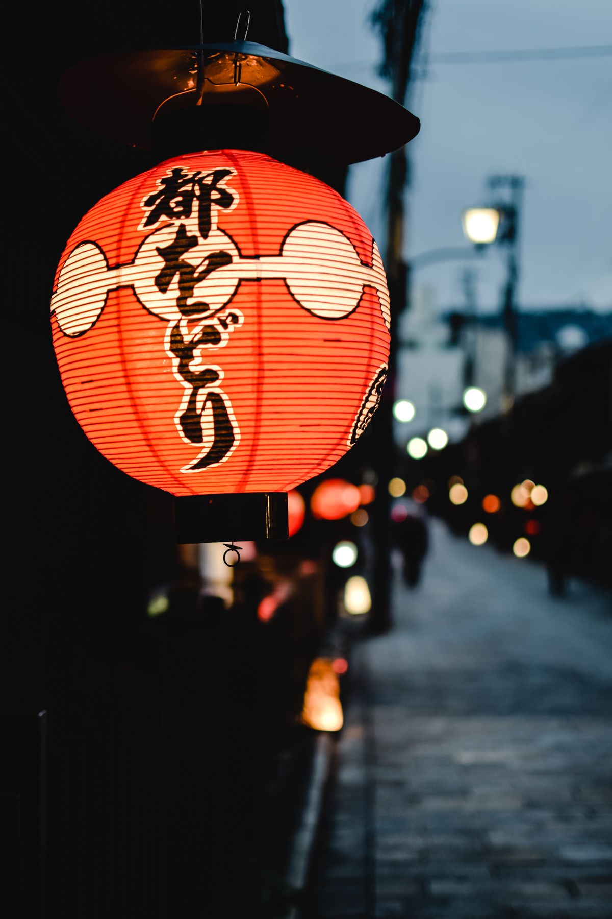 A glowing red paper lantern at the entrance to a Japanese alley at night, in a traditional hot spring district