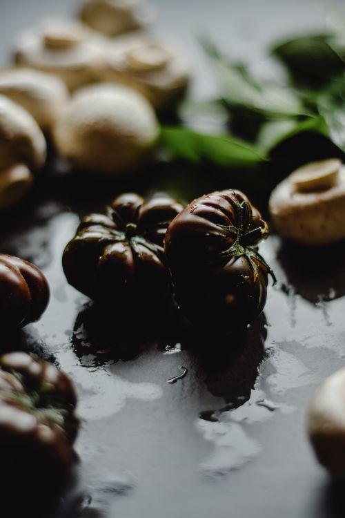 Free Wet mushrooms and heirloom tomatoes arranged on a dark surface with leafy greens. Stock Photo