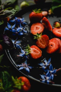 Vertical shot of sliced strawberries and blue borage flowers on a dark plate, exuding a fresh and healthy vibe.