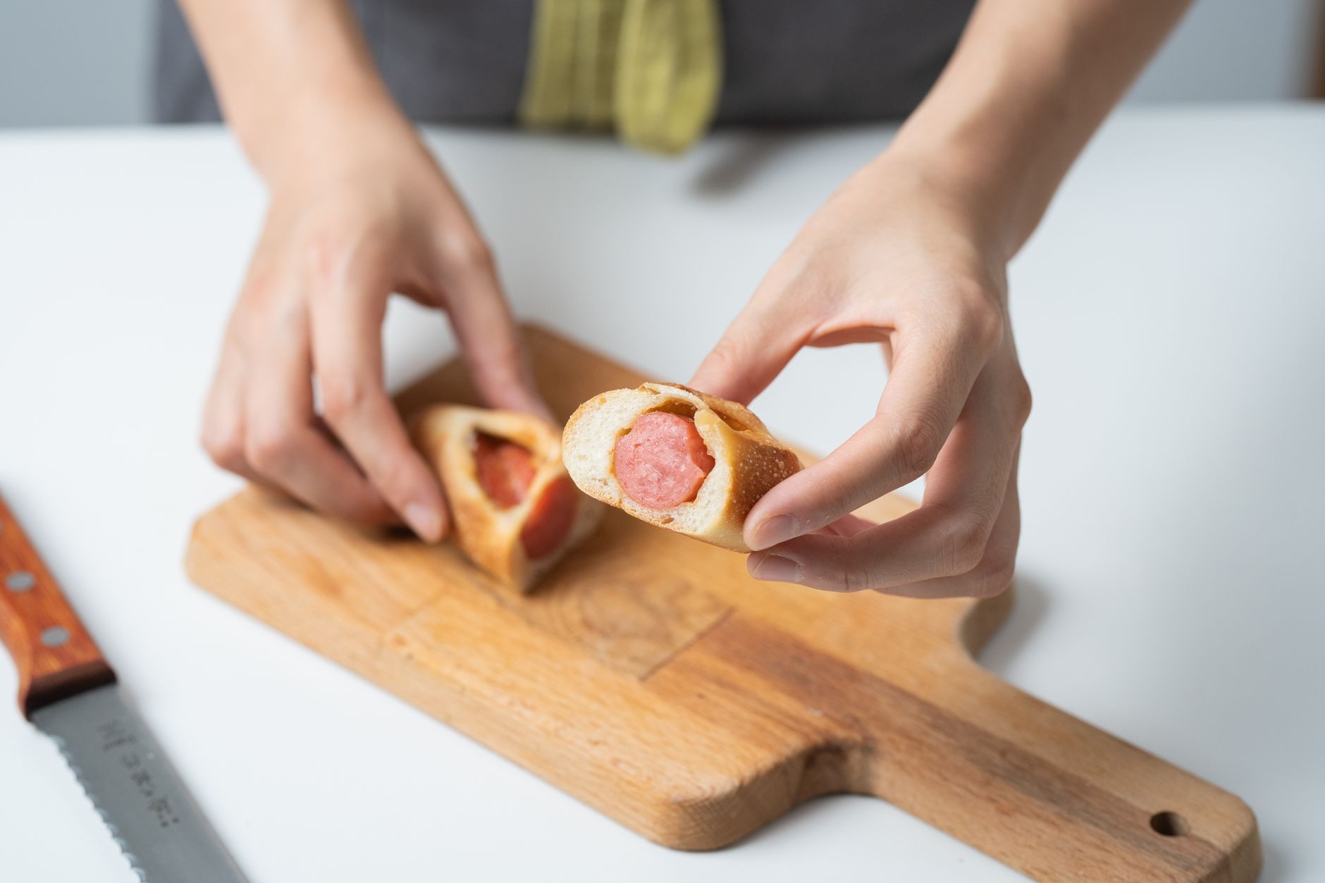 Close-up of hands holding freshly baked sausage rolls on a wooden board.