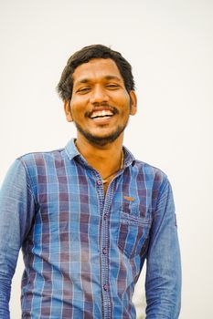 A cheerful man wearing a plaid shirt, smiling broadly against a plain background.