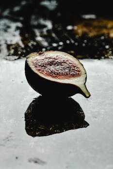 Moody artistic shot of a halved fig on a textured wet surface, adding a dark, intriguing ambiance.
