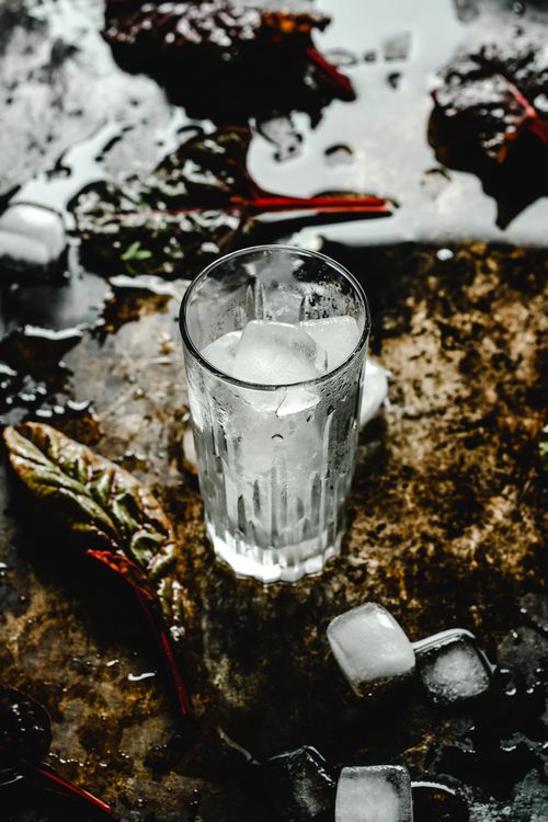 Free A refreshing cold drink with ice cubes on a rustic, wet surface surrounded by leaves. Stock Photo