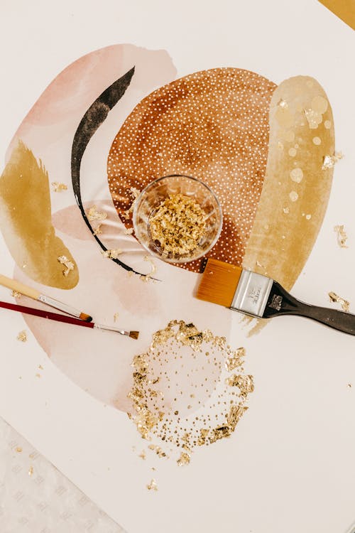 Top view of various paintbrushes and glass with gold powder placed on abstract image