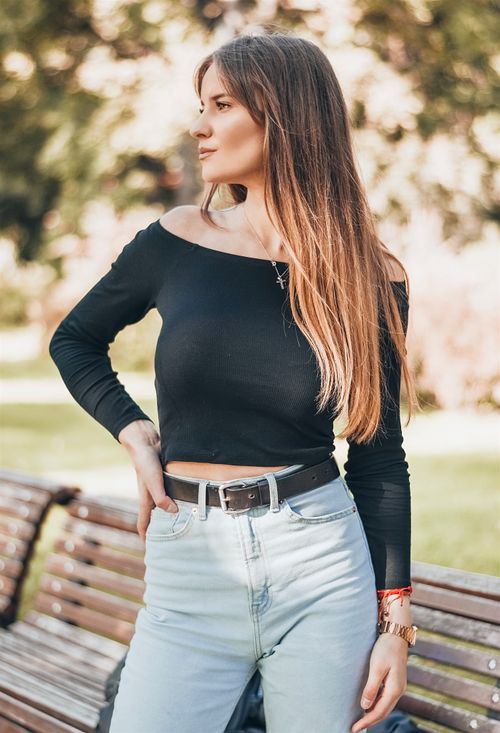 Free Fashionable young woman wearing black long-sleeve top and jeans, posing outdoors on a park bench. Stock Photo