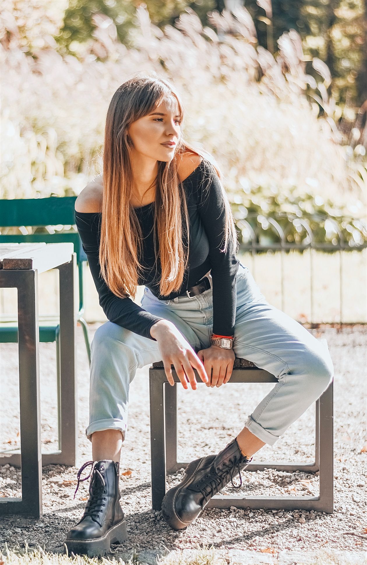 Woman in a black off-shoulder top and light-wash cuffed jeans with black lace-up ankle boots