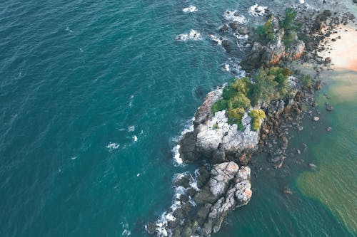 From above of rocky cliff surrounded with deep turquoise endless water of ocean