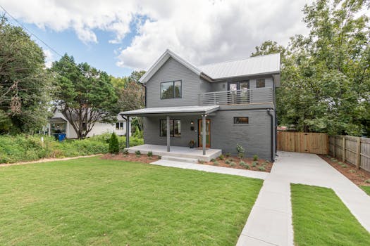 A contemporary two-story gray house with a well-maintained garden and lush green lawn.