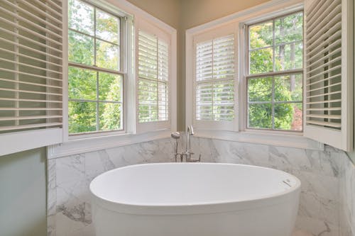 White Ceramic Bathtub Near Wooden Windows with Shutters