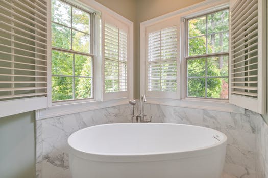 Elegant bathroom featuring a marble design and a freestanding tub, with natural light flooding through large windows.