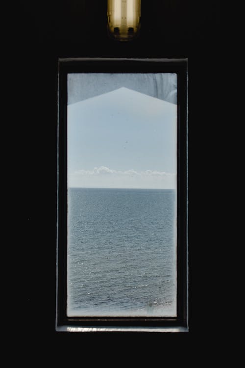 View of light blue sky with clouds over endless ocean from long narrow rectangular window in dark room