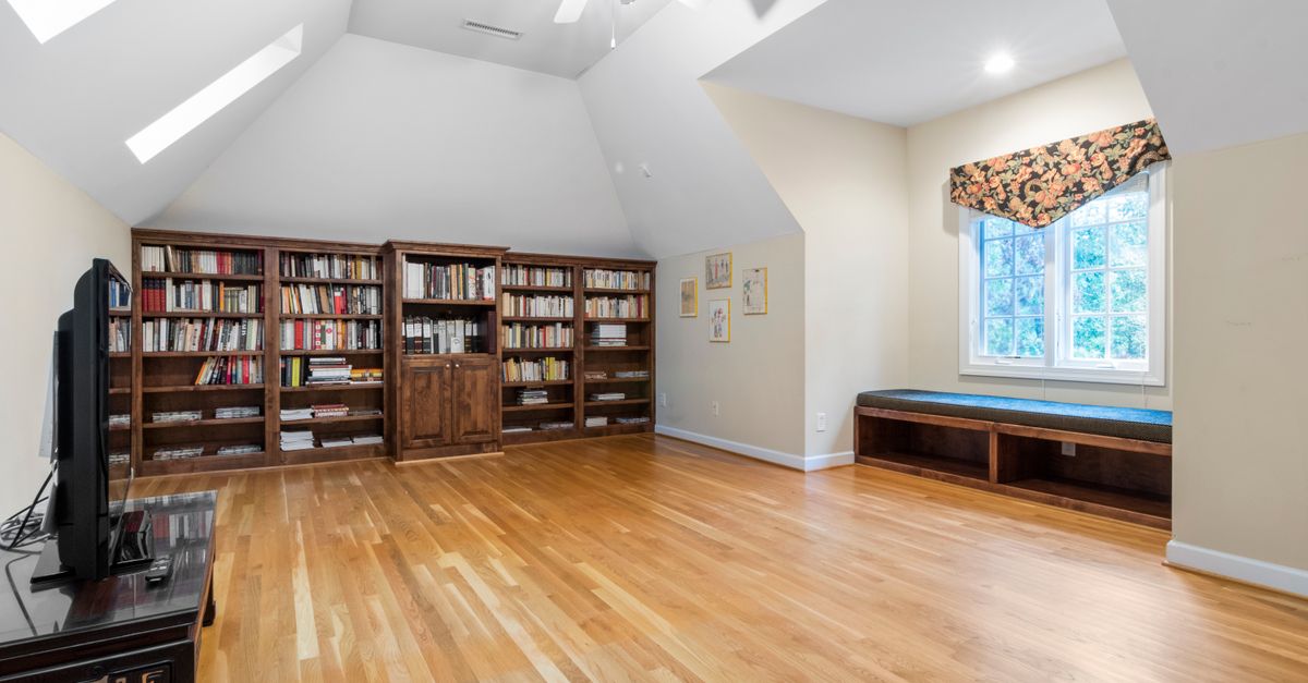 Bright attic room with wooden floors, large bookcase, and natural light through skylights.