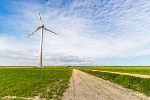 Free A windmill stands tall in a lush green field under a blue sky, capturing renewable energy. Stock Photo