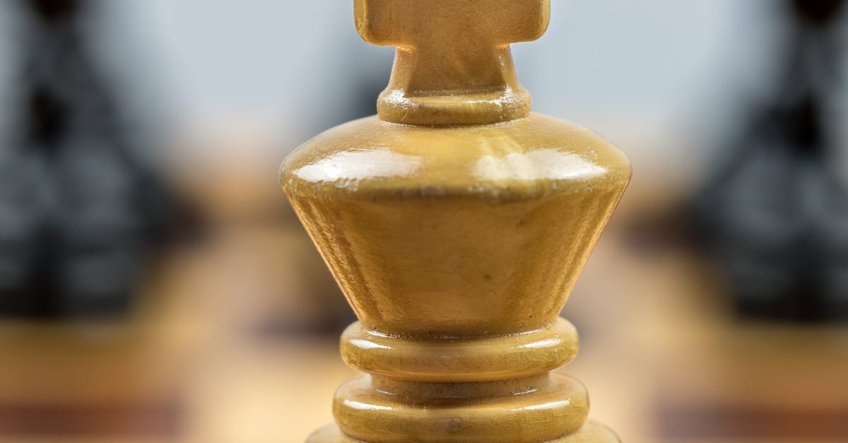 Detailed view of a wooden chess king piece on a chessboard with blurred pieces in the background.