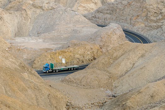 A blue truck drives through a winding road in a rocky mountain landscape, showcasing remote travel.