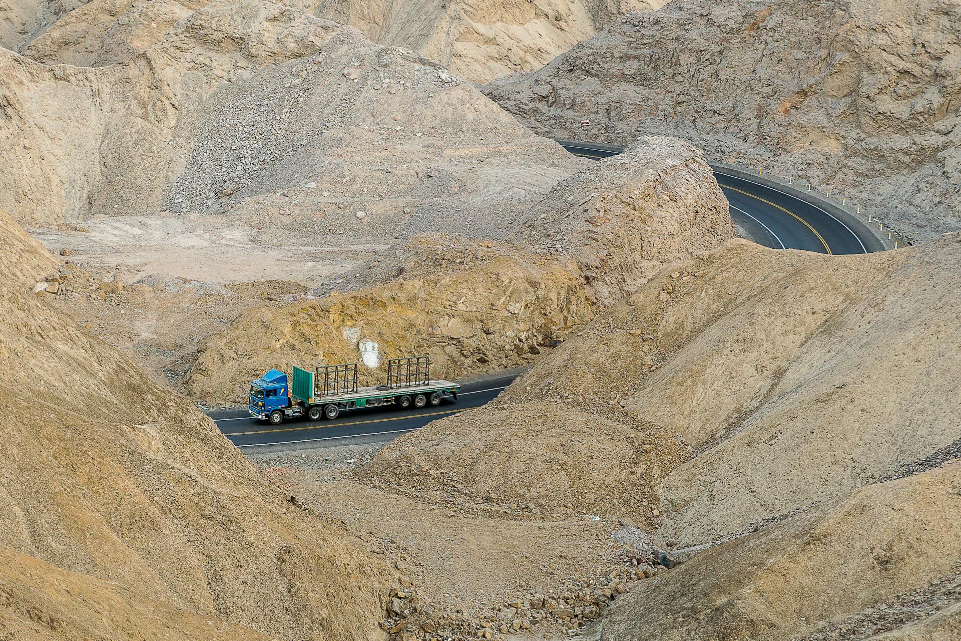 A blue truck drives through a winding road in a rocky mountain landscape, showcasing remote travel.