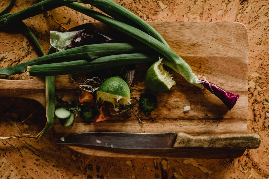 A rustic display of fresh vegetables including lime and leeks on a wooden chopping board, ideal for healthy cooking.