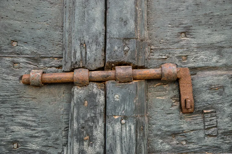 Verrou à targette en fer rouillé posé en applique sur une porte en bois