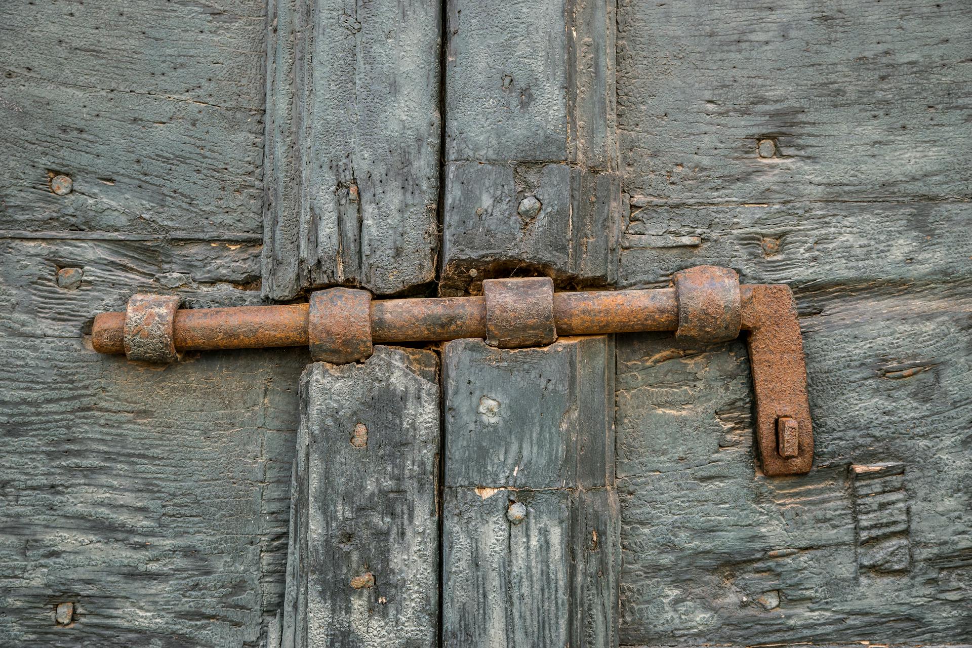 Detailed shot of a corroded iron bolt lock on a weathered wooden door.