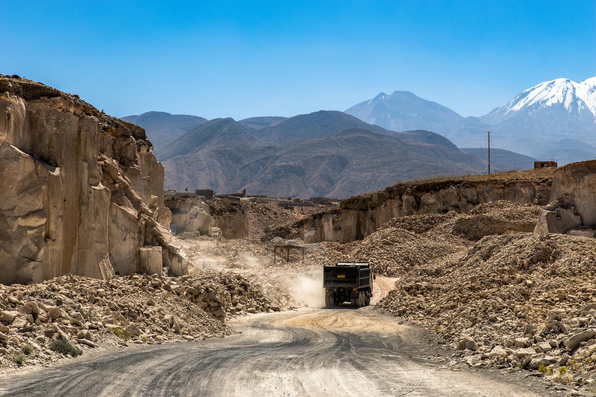 A dusty truck on a winding road through rocky mountains showcasing rugged terrain and clear blue skies.