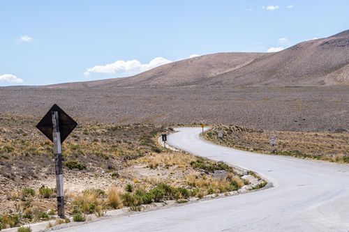 Free A quiet, curved highway cuts through a barren desert landscape beneath a clear blue sky. Stock Photo