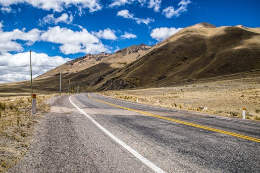 A deserted highway runs alongside scenic mountains under a bright blue sky.