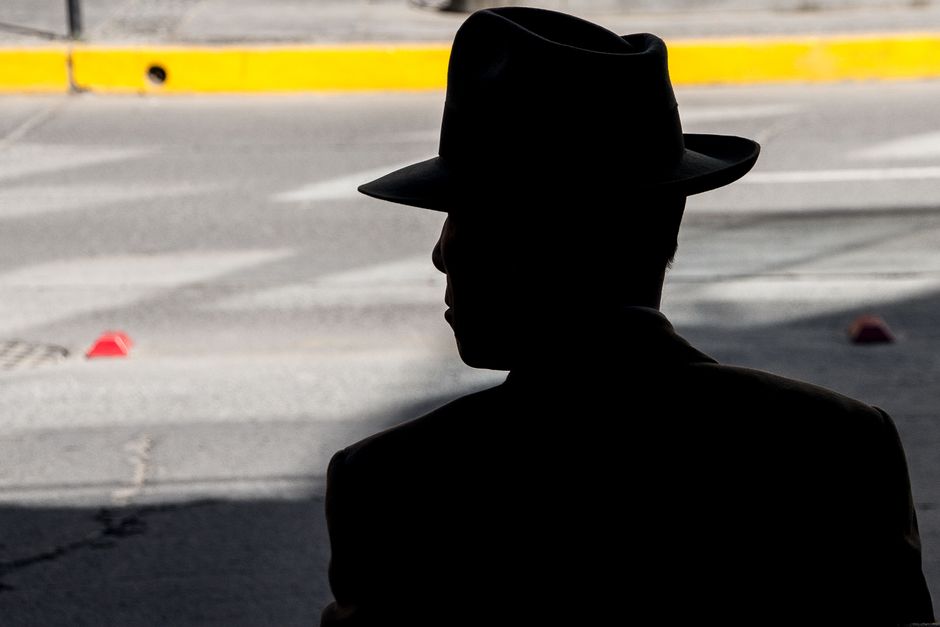 Shadowed silhouette of a man wearing a hat, captured in an urban street setting.
