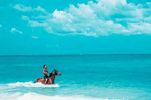 Free A man rides a horse through the vibrant turquoise waters of San Andrés beach, capturing a moment of serene adventure. Stock Photo