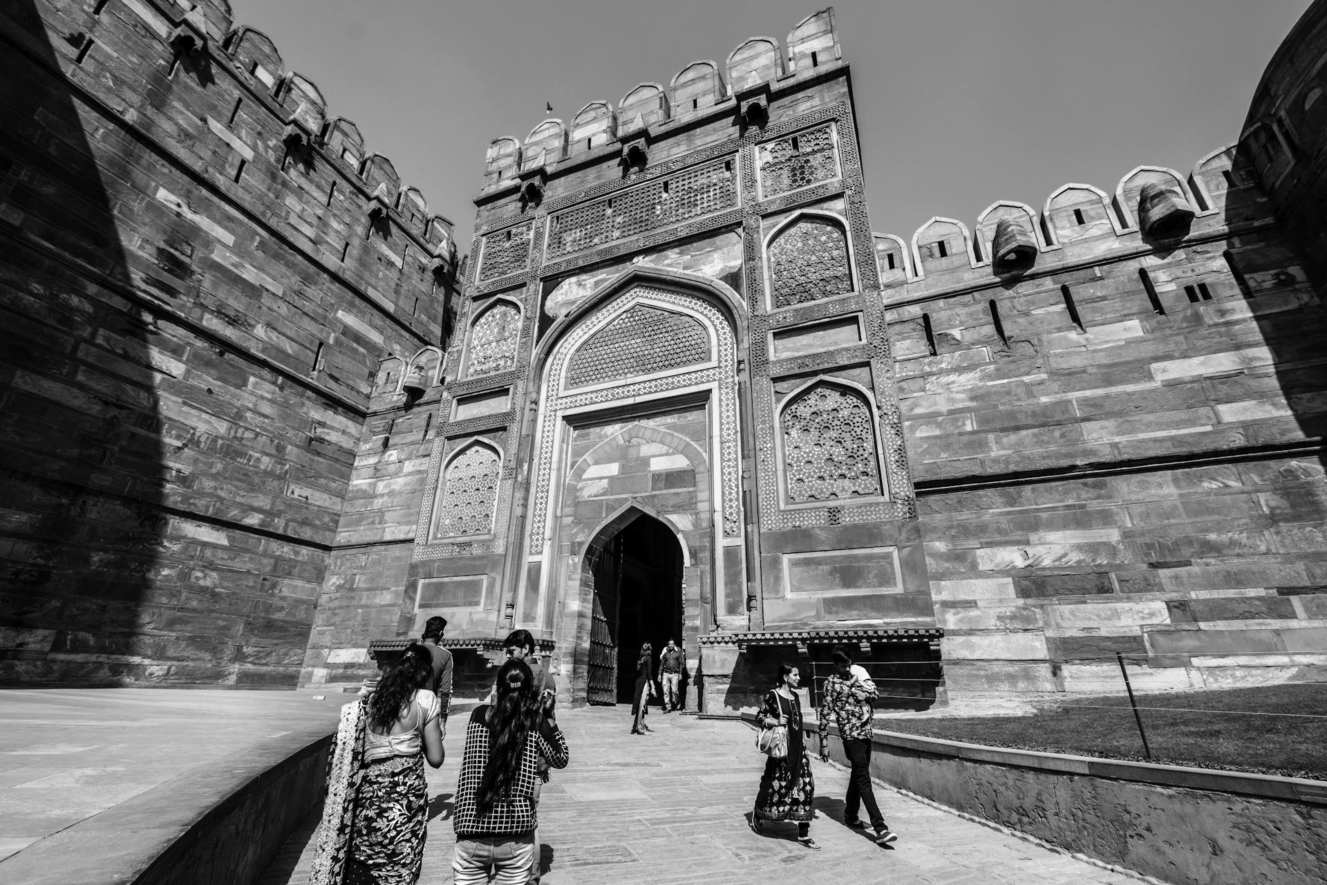 Visitors walking towards the historic Agra Fort gateway in India, captured in monochrome.