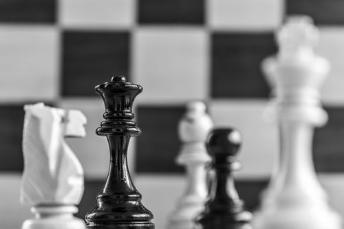 Free A focused view of a black queen chess piece with blurred chessboard background. Stock Photo