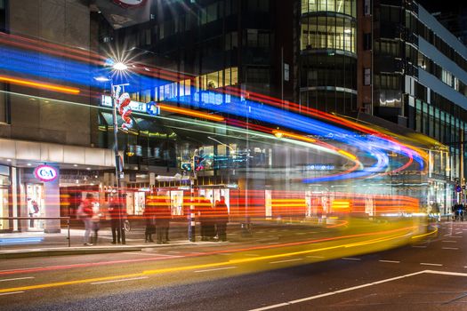 Vibrant city street scene at night showcasing colorful light trails and blurred motion in an urban setting.