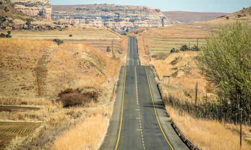 Free A long road stretches through a barren countryside with distant hills and a canyon under a clear sky. Stock Photo
