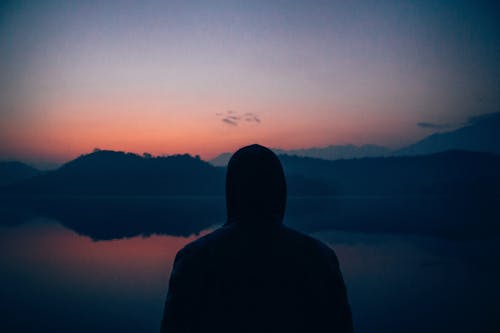 Silhouette of a Person with a Hoodie Looking at the Lake