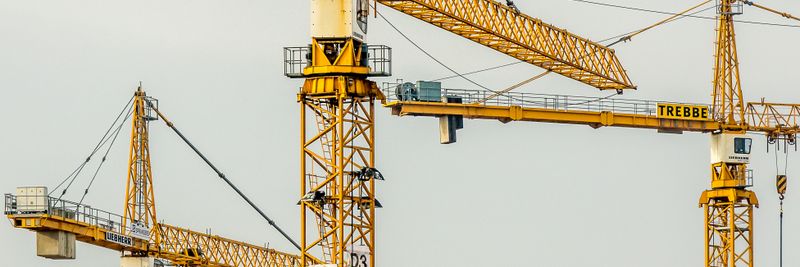 Cluster of yellow tower cranes at a construction site with a gloomy sky background.