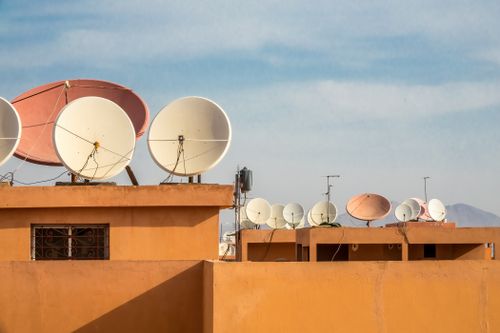 Free Multiple satellite dishes on orange rooftops under a clear blue sky, capturing urban connectivity. Stock Photo