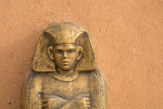 A close-up of an ancient Egyptian style statue against a textured wall.