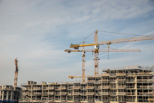 Modern construction site with cranes against blue sky, showcasing urban development.