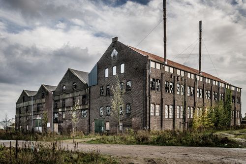 Free Large abandoned warehouse with a weathered exterior and broken windows. Stock Photo