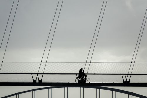 Free Minimalistic silhouette of a couple biking on a modern bridge against the sky. Stock Photo