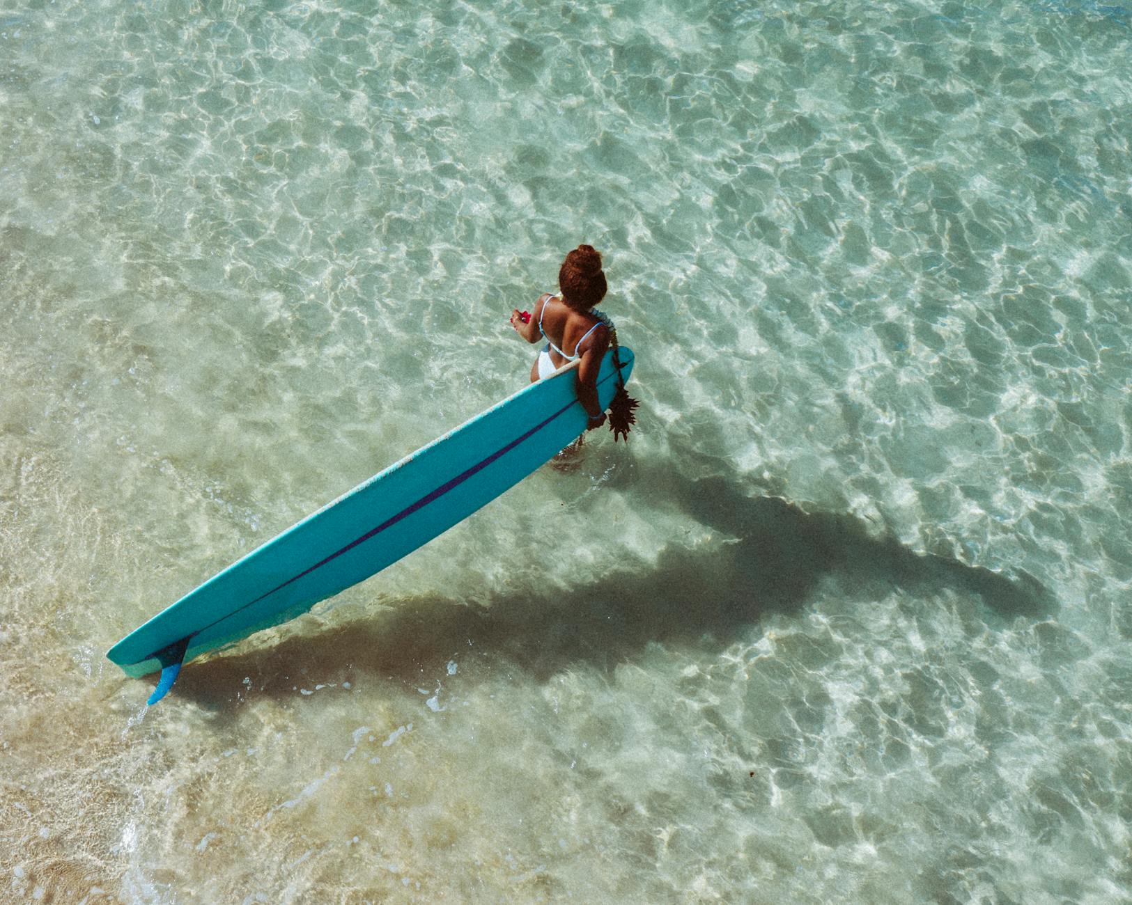 A woman in swimwear holding a surfboard in crystal-clear ocean water, ready to surf.