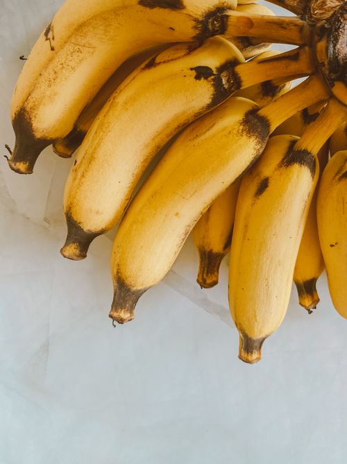 Free A vertical shot of ripe bananas clustered together on a marble surface, showing natural imperfections. Stock Photo