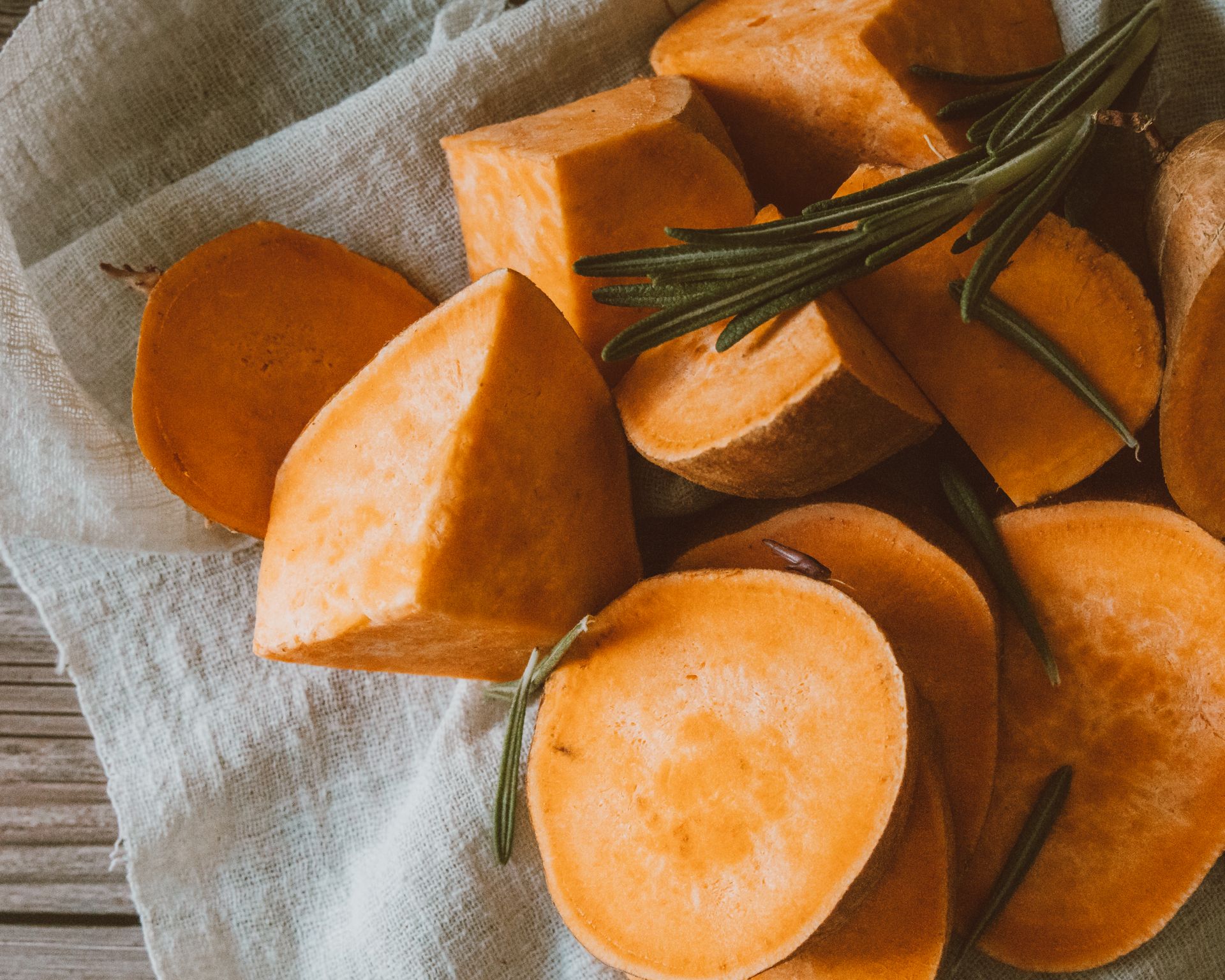 Close-up of sliced sweet potatoes with rosemary on cloth background.