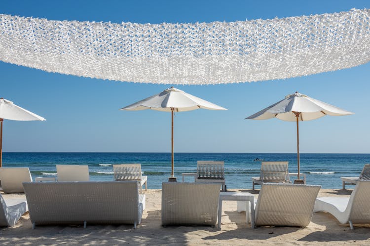 White Patio Umbrellas With Beach Chairs And Tables Near The Seashore